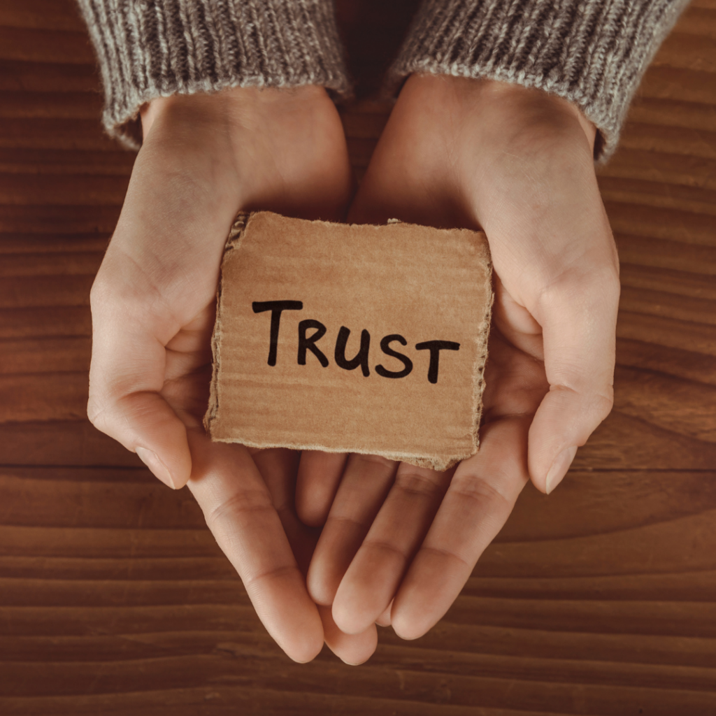 Woman holding a piece of cardboard with the word trust written on it
