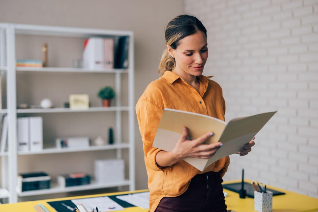 Woman in office wearing orange shirt and holder large folder.

Pexels: search female professional speaking meeting